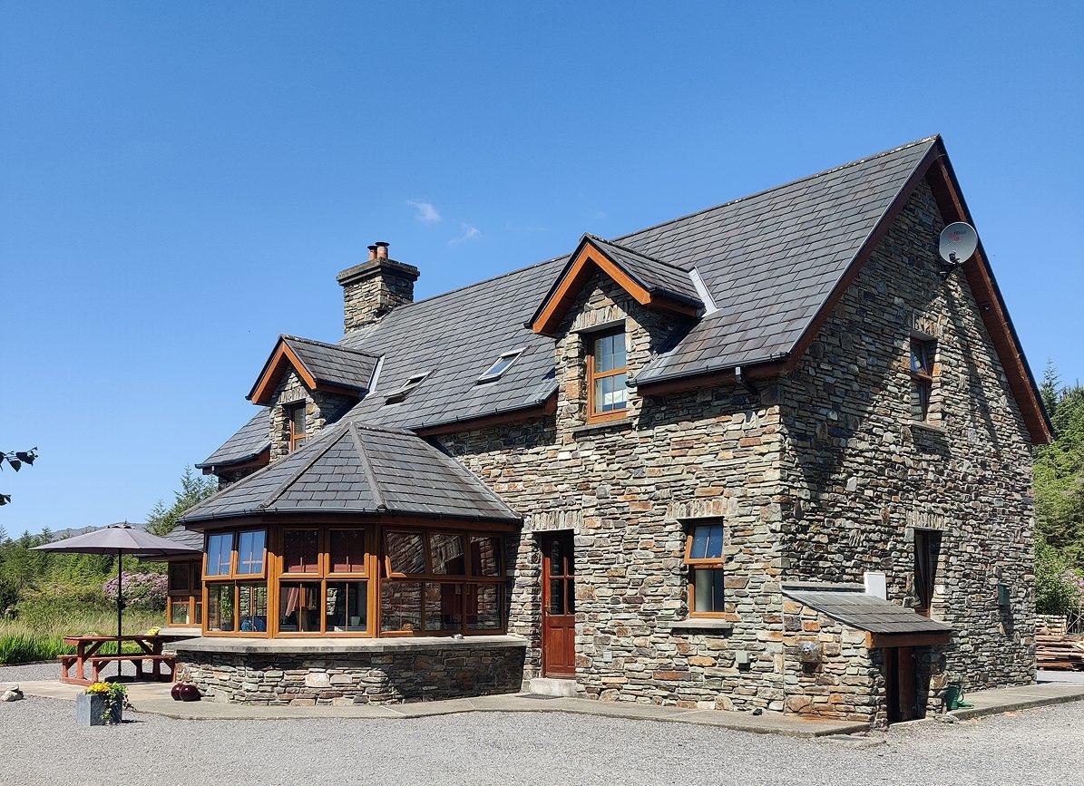Stone house with a slate roof, dormer windows and a glass-enclosed porch under a clear blue sky